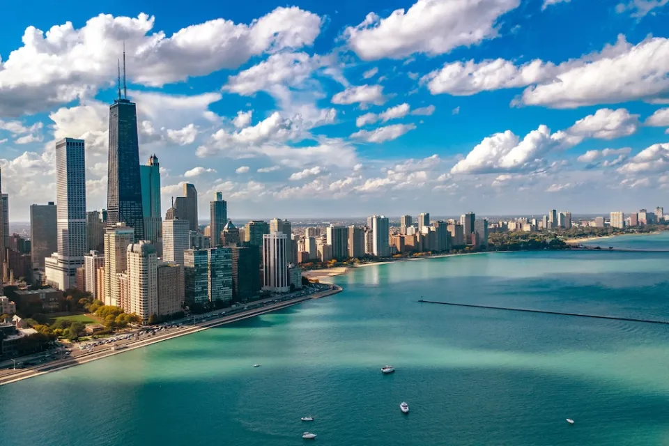 Aerial view of Chicago skyline on bright day with turquoise Lake Michigan in foreground.